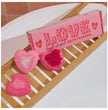 Heart-shaped bath fizzers with a pink box labeled 'LOVE' on a wooden tray.