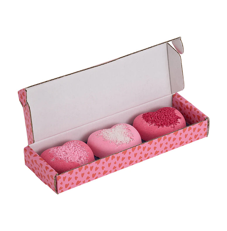 Three pink heart-shaped bath bombs in a box with a heart pattern on a white background