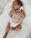 Newborn baby lying on a white blanket with a wooden disc that says 'Hi Hello World'.