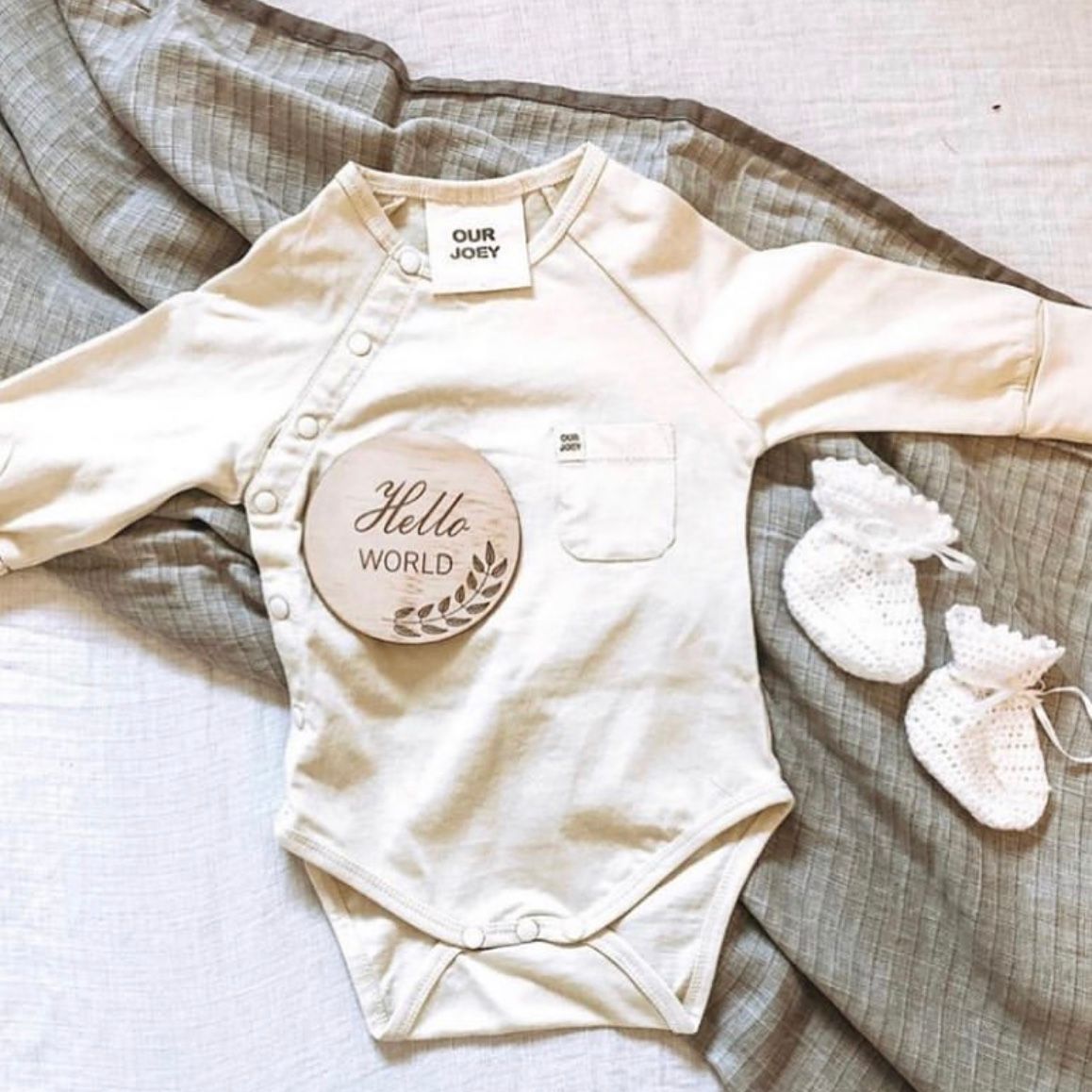 Baby onesie with 'Hello World' patch and baby booties on a textured surface
