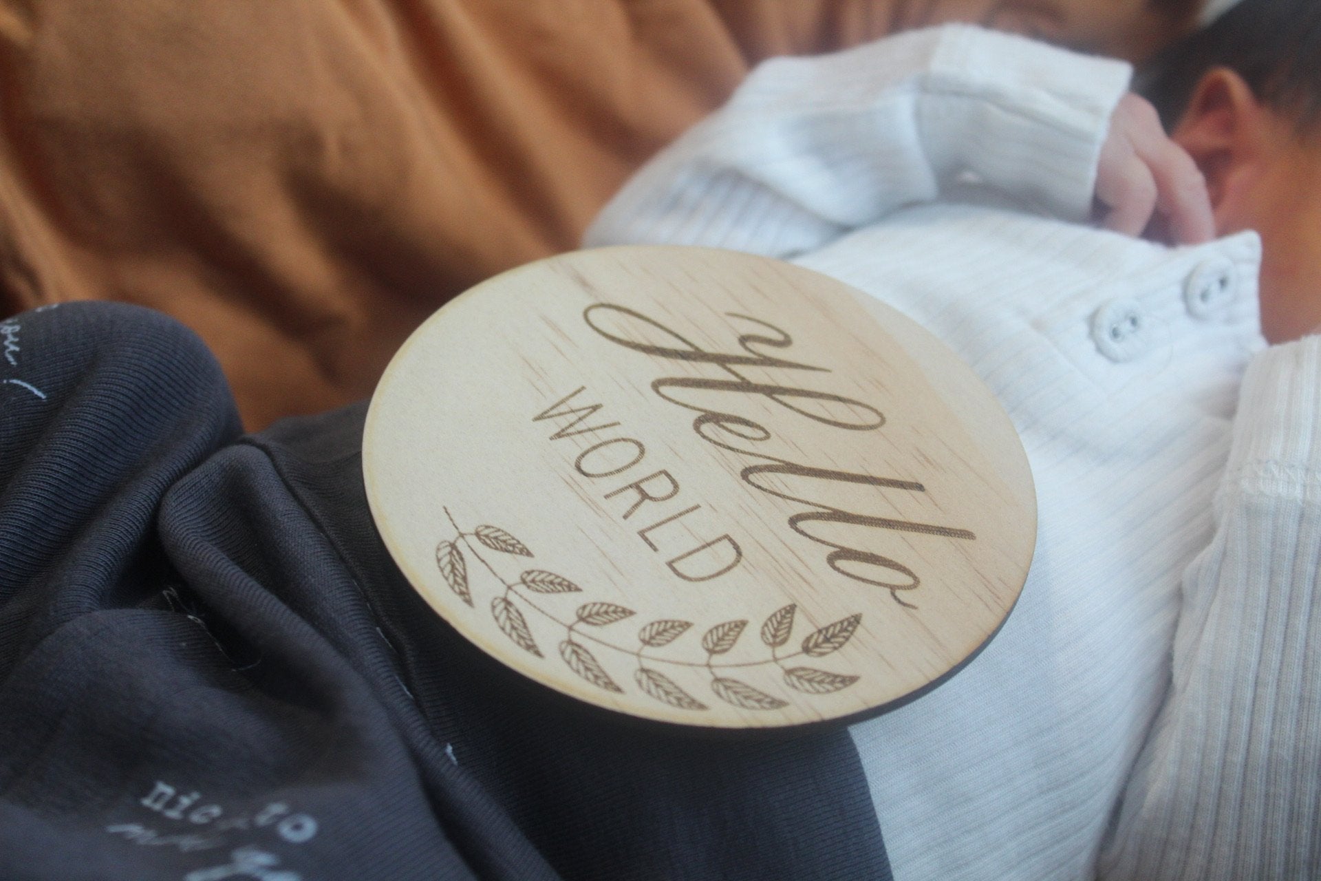 Round wooden sign with 'Hello World' engraving held by a person