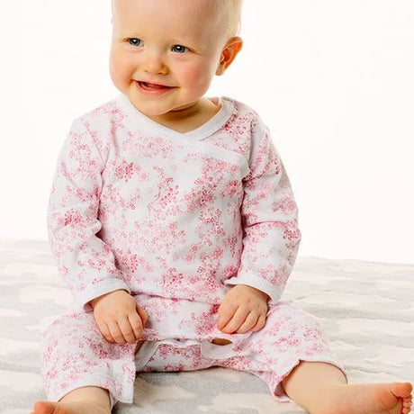 Baby wearing a white outfit with red floral pattern sitting on a white surface