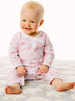 Baby wearing a white outfit with red floral pattern sitting on a white surface