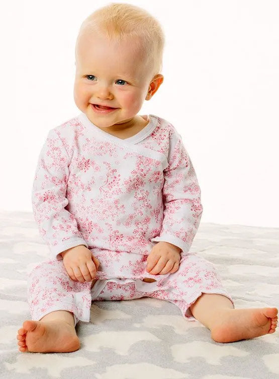 Baby wearing a white outfit with red floral pattern sitting on a white surface