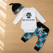 Baby outfit set with white long-sleeve onesie, black hat, and blue pants with black stormtropper patterns on a table background.