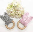 Two knitted baby teething rings, one gray and one pink, with wooden rings on a white background.