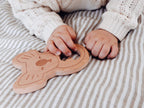 Child's hands holding a wooden teething toy on a striped fabric background