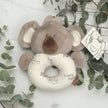 Plush koala toy with a ring on a wooden surface with greenery