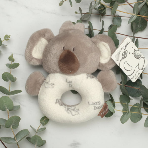 Plush koala toy with a ring on a wooden surface with greenery
