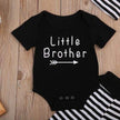 Black baby onesie with 'Little Brother' text on a wooden surface