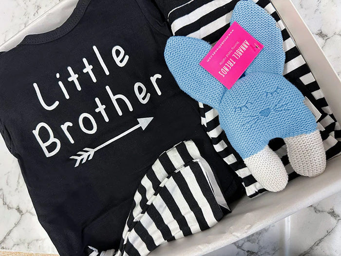 Black 'Little Brother' onesie with a gray stuffed animal on a marble surface
