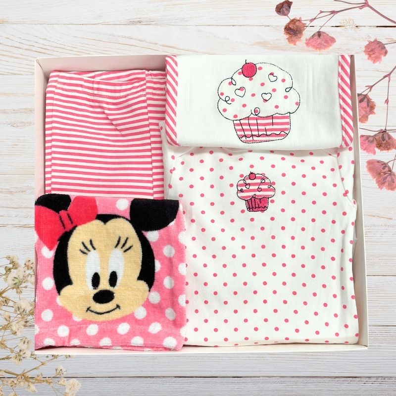 Set of baby girl clothes with Minnie mouse designs in a gift box on a wooden surface