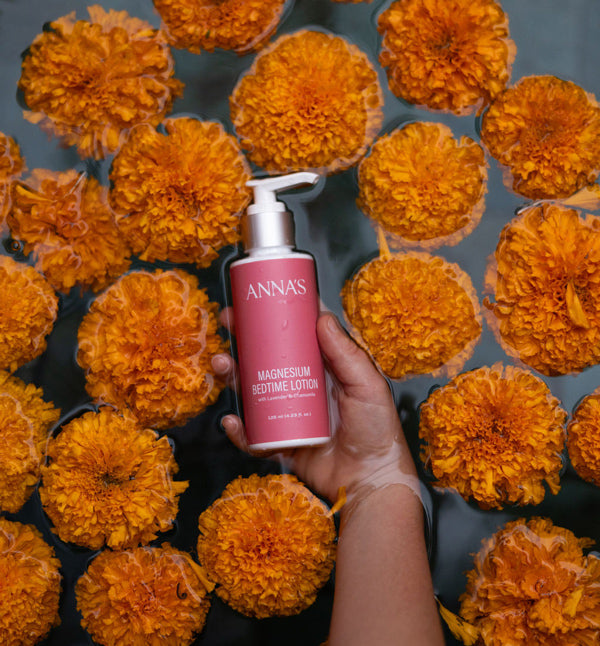 Person holding a pink bottle labeled 'Anna's' around flowers