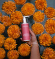 Person holding a pink bottle labeled 'Anna's' around flowers
