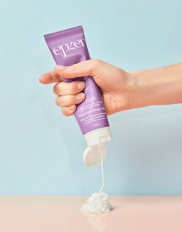 Hand holding a tube of Epzer body lotion against a light blue background