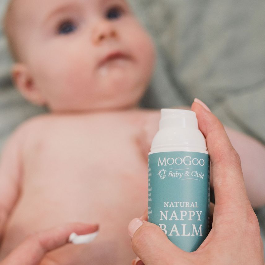 Person holding a bottle of MooGoo Natural Nappy Balm in front of a baby