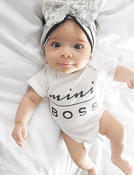 Baby wearing a 'mini boss' onesie and a decorative headband on a white background