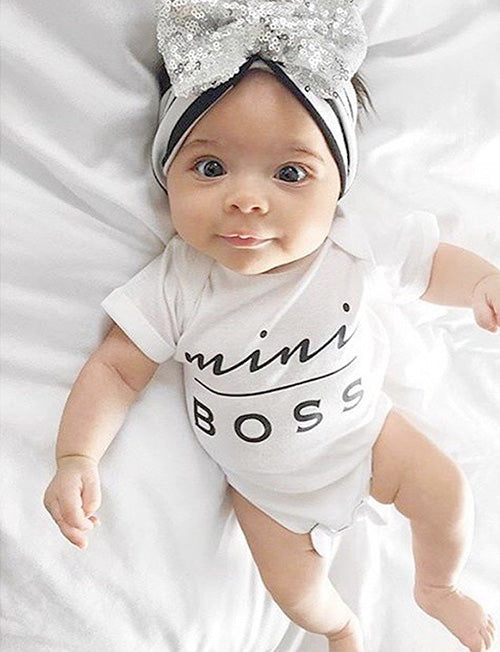Baby wearing a 'mini boss' onesie and a decorative headband on a white background