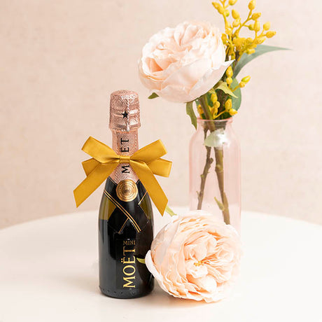 Moét champagne bottle with a gold bow and flowers on a light background