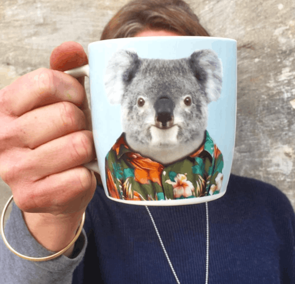 Person holding a mug with a koala wearing a floral shirt design.