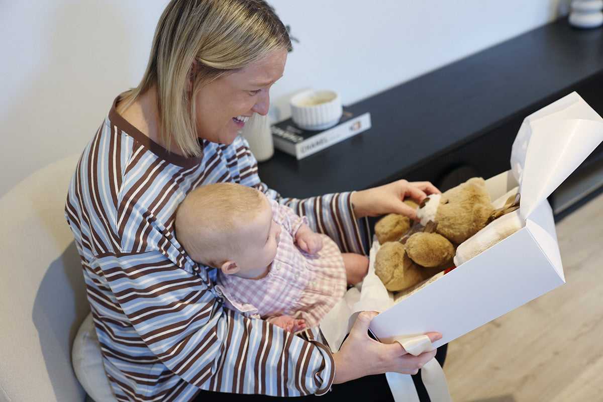 New mother smiling and baby girl opening a baby gift box