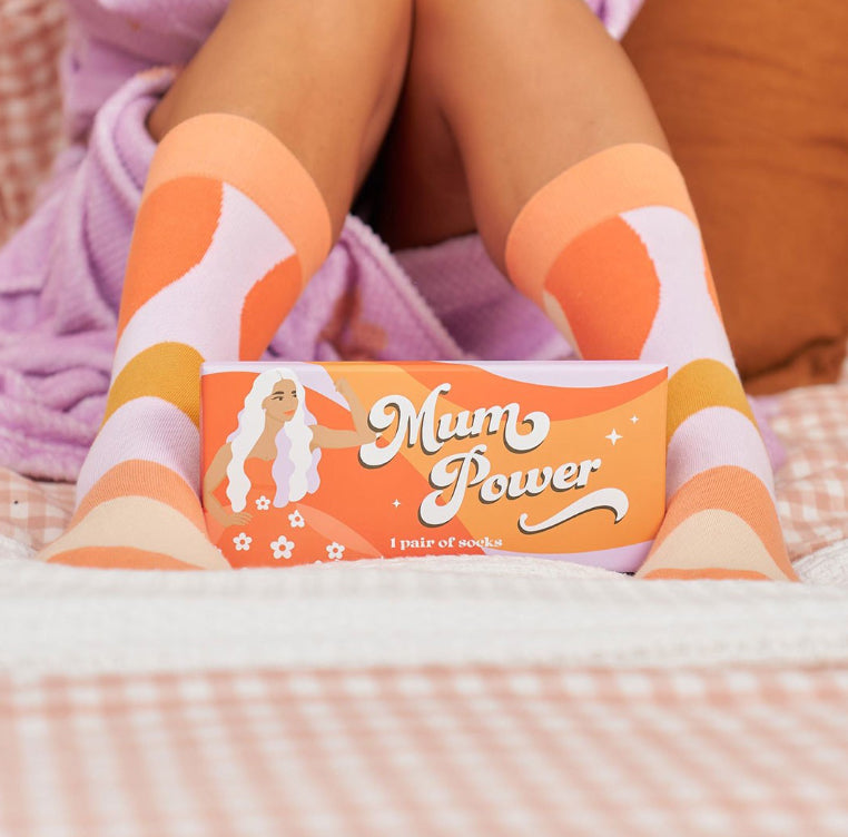 Person wearing orange and white socks with 'Mum Power' packaging.