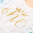White baby romper with gold 'she' and crown design on a light blue background