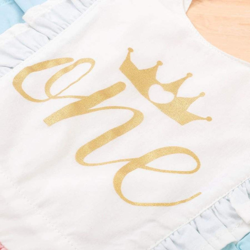 White baby romper with gold 'she' and crown design on a light blue background