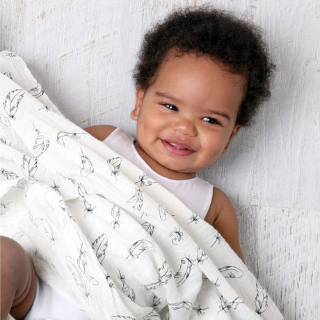 Baby wrapped in a white blanket with black patterns, smiling against a light wooden background