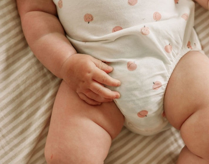 Baby wearing a white onesie with pink fruit patterns on a striped background
