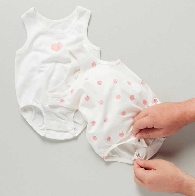 White baby romper with pink peach patterns on a gray background