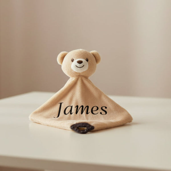 Plush bear-shaped comfort blanket with 'James' printed on table