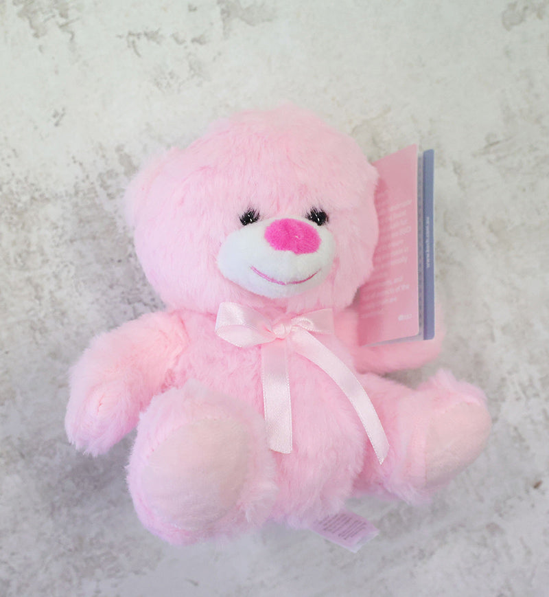 Pink teddy bear with a white bow on a light gray background