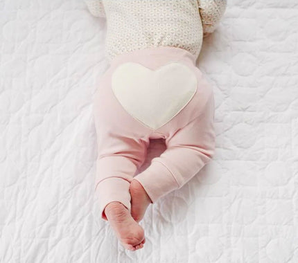 Baby wearing pink pants with a heart design on a white blanket
