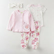 Baby clothing set with pink cardigan, white onesie with swan design, and floral pants on a white background.