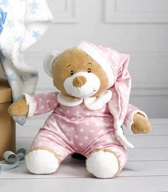 Teddy bear in a pink outfit with white polka dots on a light wooden floor.