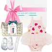 Baby gift set with pink onesie, shoes, and other items from The Baby Gift Company.