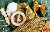 Baby toys and items including a wooden rattle, knitted toy, and bow on green leaves.