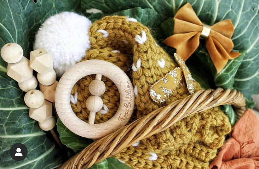 Baby toys and items including a wooden rattle, knitted toy, and bow on green leaves.