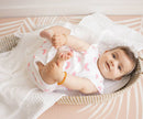 Baby lying on a white blanket with pink accents in a crib