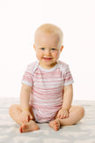 Baby wearing a striped onesie sitting on a white surface
