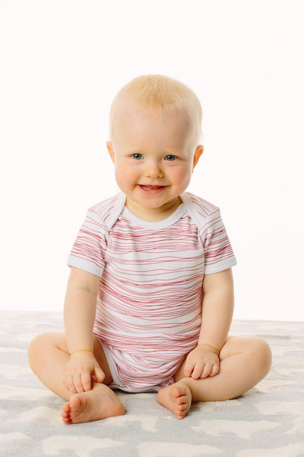 Baby wearing a striped onesie sitting on a white surface