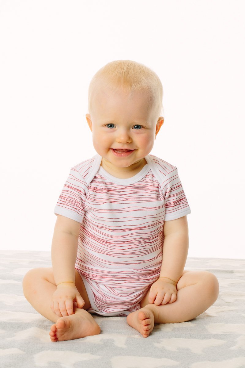 Baby wearing a striped onesie sitting on a white surface