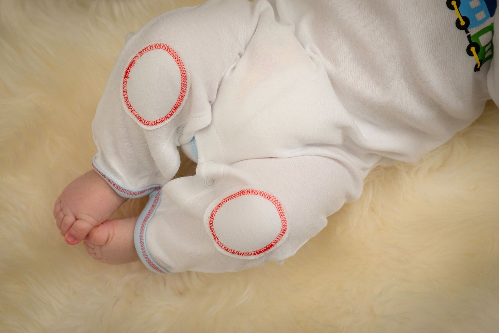 Baby's legs in white pants with red circles on a beige surface