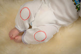 Baby's legs in white pants with red circles on a beige surface