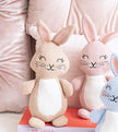 Three crocheted bunny toys on a pink surface with a blurred background