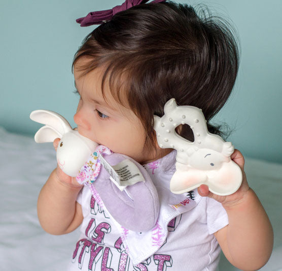 Baby holding two teething toys against a light blue background
