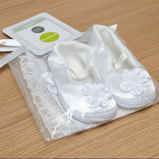 White baby shoes with floral details in a clear bag, on a wooden table