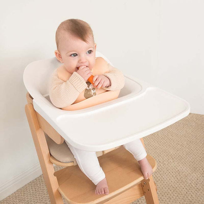Baby eating a carrot whilst wearing a bib in a high chair