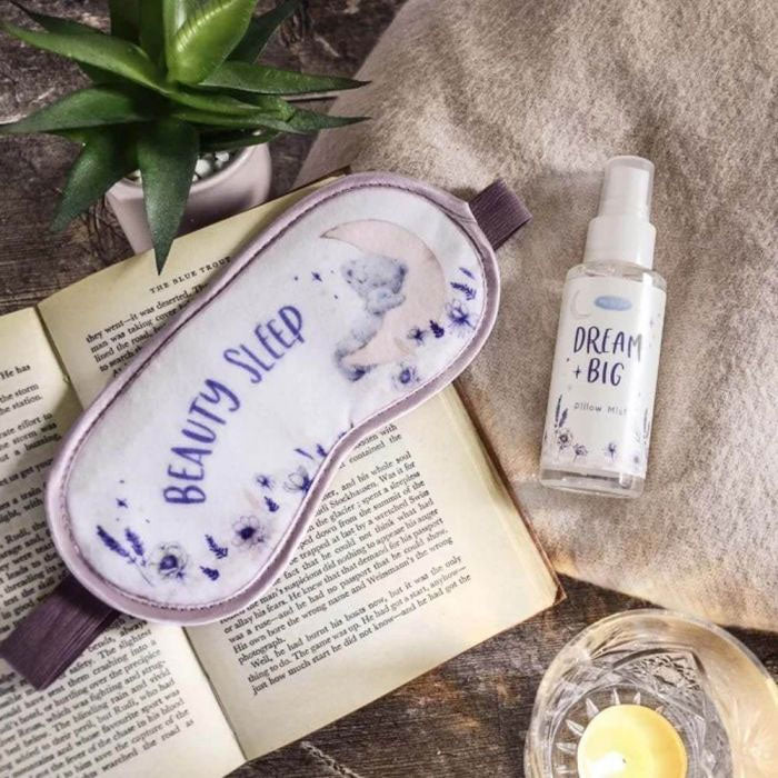 Sleep mask and bottle labeled 'Dream Big' on an open book with a plant and candle in the background.